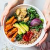 Woman hands eating vegan salad of baked vegetables, avocado, tofu and buckwheat buddha bowl, top view. Plant based food concept.